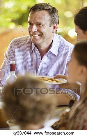 Picture - Family having meal and discussing at dining table. Fotosearch