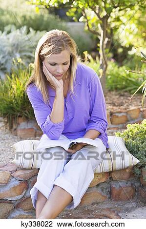 Beautiful young woman reading book in garden with hand on chin View Large Photo Image Stock Image - Beautiful young woman reading book in garden with hand on chin. Fotosearch