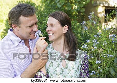 Stock Image - Happy mature couple smelling flowers in the garden. Fotosearch