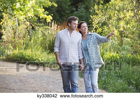 Stock Image - Happy mature couple walking in a garden. Fotosearch
