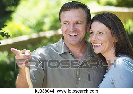 Smiling man showing something to his wife outdoors View Large Photo Image Picture - Smiling man showing something to his wife outdoors. Fotosearch
