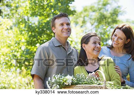 Picture - Woman standing with his son and daughter in law while holding basket of flowers. Fotosearch