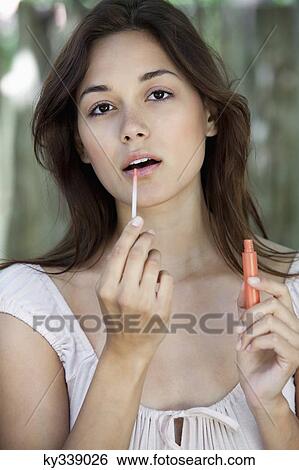 Stock Photograph - Portrait of a beautiful young woman applying lip gloss. Fotosearch