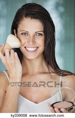 Portrait of a woman applying powder compact on her face View Large Photo Image Stock Photo - Portrait of a woman applying powder compact on her face. Fotosearch