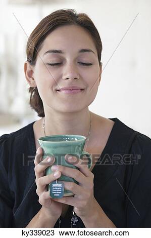 Young woman holding cup of tea with her eyes closed View Large Photo Image Stock Image - Young woman holding cup of tea with her eyes closed. Fotosearch