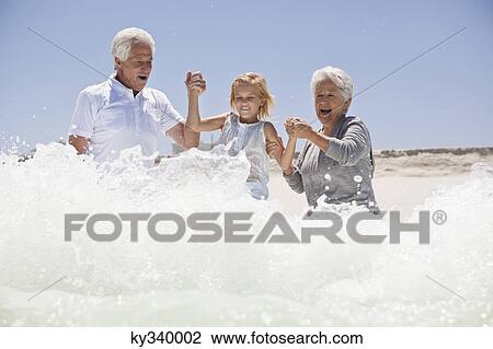 Stock Image - Girl enjoying on the beach with her grandparents. Fotosearch