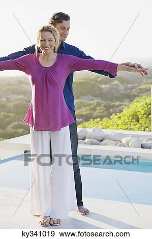 Stock Photo - Mid adult couple standing at the poolside and smiling. Fotosearch