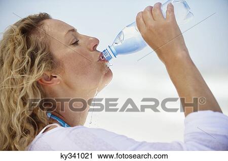Stock Image - Side profile of a beautiful woman drinking purified water. Fotosearch