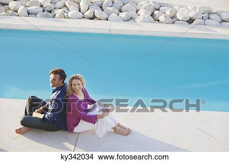 Mid adult couple sitting back to back at the poolside View Large Photo Image Picture - Mid adult couple sitting back to back at the poolside. Fotosearch