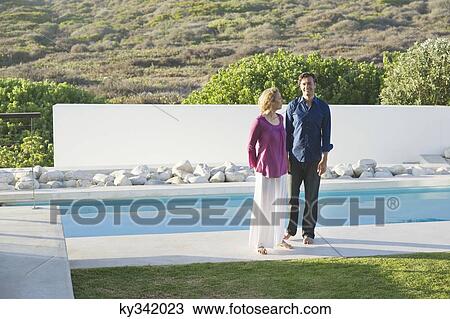 Mid adult couple standing at the poolside View Large Photo Image Stock Image - Mid adult couple standing at the poolside. Fotosearch