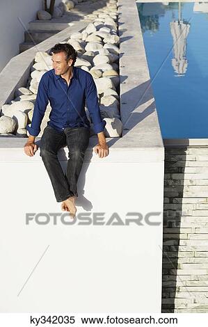 Mid adult man sitting on the terrace near a swimming pool View Large Photo Image Stock Photography - Mid adult man sitting on the terrace near a swimming pool. Fotosearch