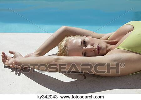 Stock Image - Woman sunbathing at poolside. Fotosearch
