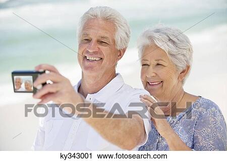 Stock Image - Happy senior couple taking a picture of themselves with a digital camera. Fotosearch