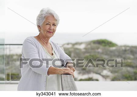 Stock Image - Portrait of a senior woman standing at a balcony and smiling. Fotosearch