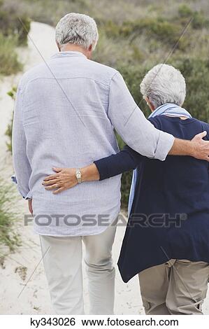Rear view of a senior couple walking on the beach with their arms around each other View Large Photo Image Stock Photograph - Rear view of a senior couple walking on the beach with their arms around each other. Fotosearch