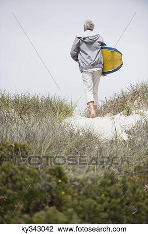 Rear view of a senior man carrying surfboard on the beach View Large Photo Image Stock Image - Rear view of a senior man carrying surfboard on the beach. Fotosearch