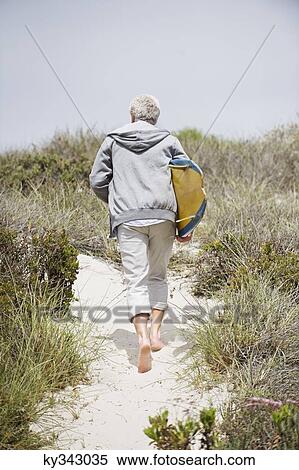 Rear view of a senior man carrying surfboard on the beach View Large Photo Image Stock Photography - Rear view of a senior man carrying surfboard on the beach. Fotosearch