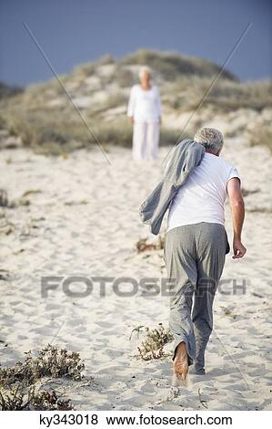 Rear view of a senior man running towards a woman standing in the background View Large Photo Image Stock Photo - Rear view of a senior man running towards a woman standing in the background. Fotosearch