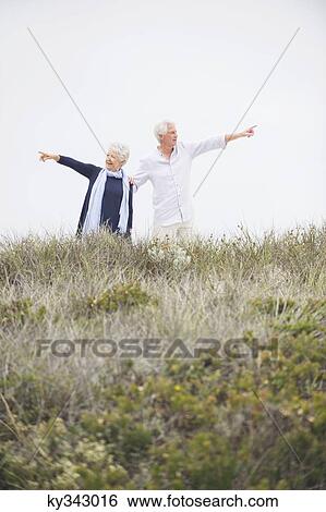 Senior couple pointing at different direction against clear sky View Large Photo Image Stock Photograph - Senior couple pointing at different direction against clear sky. Fotosearch