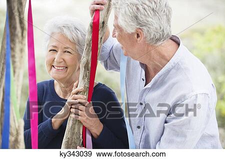 Senior couple standing near a tree decorated with ribbons View Large Photo Image Stock Photo - Senior couple standing near a tree decorated with ribbons. Fotosearch