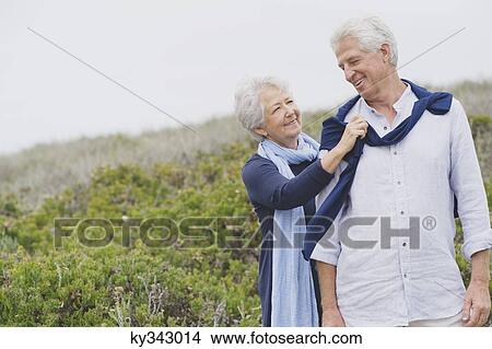 Picture - Senior woman putting sweater on husband's shoulder on the beach. Fotosearch