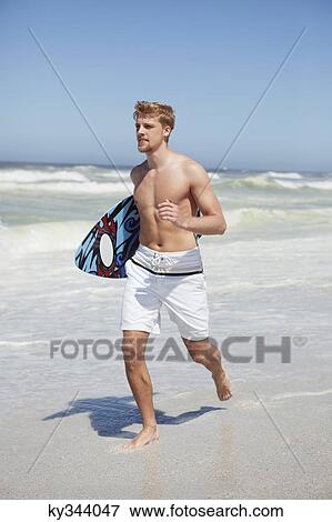Stock Photo - Man running with surfboard on the beach. Fotosearch