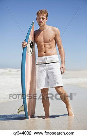 Man standing on the beach with surfboard View Large Photo Image Stock Image - Man standing on the beach with surfboard. Fotosearch