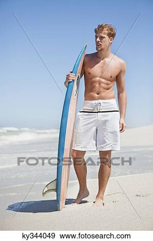 Man standing on the beach with surfboard View Large Photo Image Stock Photo - Man standing on the beach with surfboard. Fotosearch