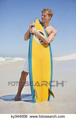 Man standing on the beach with surfboard View Large Photo Image Stock Photograph - Man standing on the beach with surfboard. Fotosearch