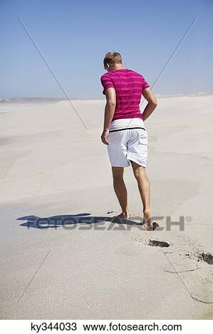 Stock Image - Rear view of a man walking on sand. Fotosearch