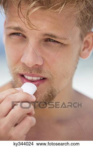 Young man applying moisturizer on his lips View Large Photo Image Picture - Young man applying moisturizer on his lips. Fotosearch