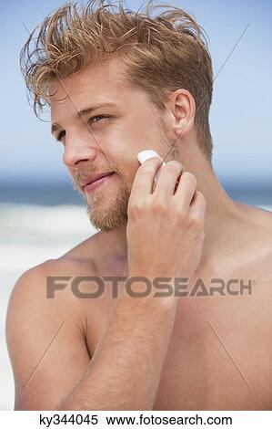 Stock Photography - Young man applying moisturizer on his face. Fotosearch