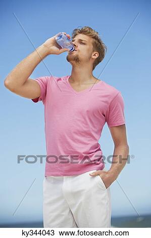 Young man drinking water from a water bottle on the beach View Large Photo Image Stock Image - Young man drinking water from a water bottle on the beach. Fotosearch