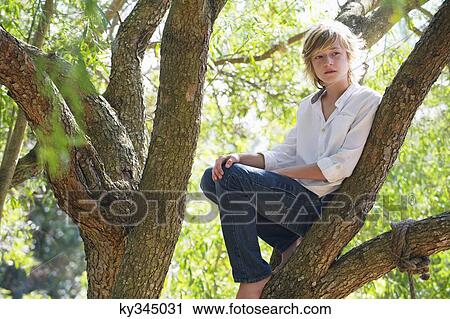 Stock Image - Contemplative little boy crouching on tree branch. Fotosearch