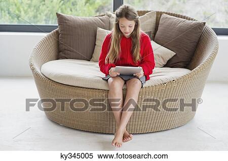 Stock Photography - Girl sitting in a wicker couch using a digital tablet. Fotosearch