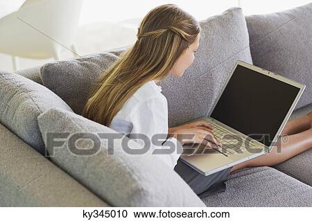 Side profile of a girl sitting on a couch and using a laptop View Large Photo Image Stock Image - Side profile of a girl sitting on a couch and using a laptop. Fotosearch