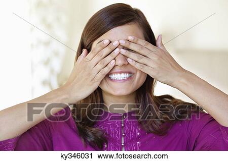 Young woman covering eyes and peeking between fingers View Large Photo Image Stock Image - Young woman covering eyes and peeking between fingers. Fotosearch