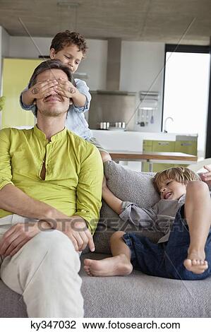 Stock Image - Boy covering his father's eyes by his brother . Fotosearch