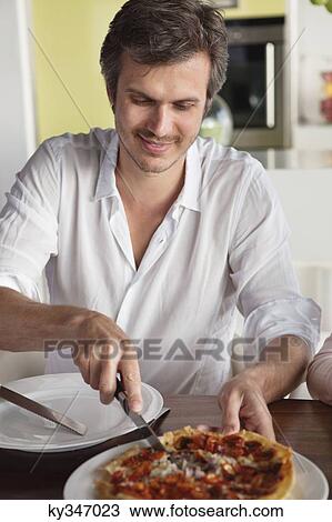 Man cutting pizza at a dining table View Large Photo Image Stock Image - Man cutting pizza at a dining table. Fotosearch