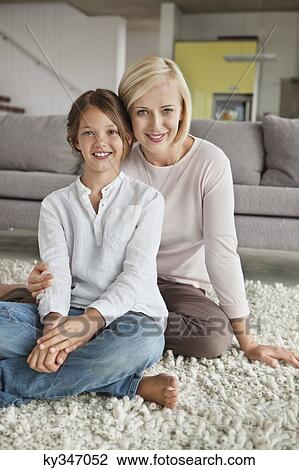 Stock Image - Portrait of a woman with her daughter sitting on carpet. Fotosearch