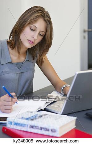 Beautiful woman writing in book while using laptop in classroom View Large Photo Image Stock Photography - Beautiful woman writing in book while using laptop in classroom. Fotosearch