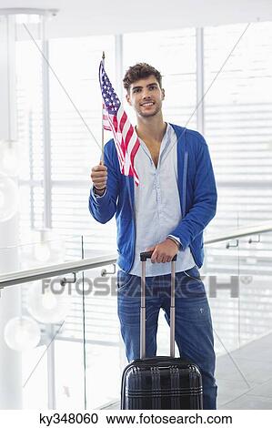 Portrait of a man holding American flag and a suitcase at an airport View Large Photo Image Stock Image - Portrait of a man holding American flag and a suitcase at an airport. Fotosearch