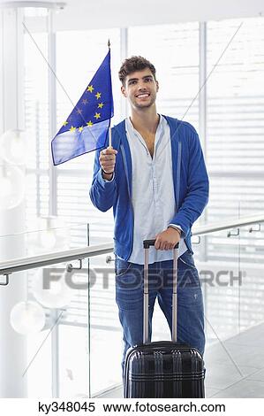 Portrait of a man holding European union flag and a suitcase at an airport View Large Photo Image Stock Photography - Portrait of a man holding European union flag and a suitcase at an airport. Fotosearch