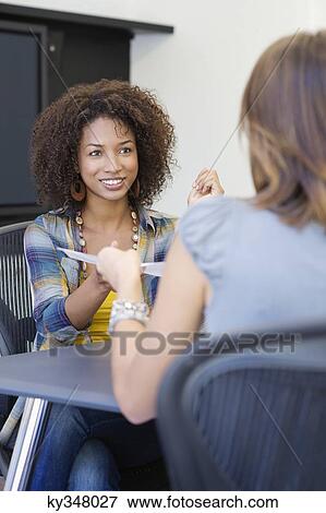 Stock Photo - Rear view of a woman giving resume to an African American woman in office. Fotosearch