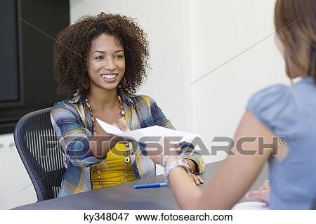 Rear view of a woman giving resume to an African American woman in office View Large Photo Image Stock Photo - Rear view of a woman giving resume to an African American woman in office. Fotosearch