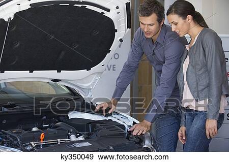 Couple looking at car engine in showroom View Large Photo Image Stock Photo - Couple looking at car engine in showroom. Fotosearch