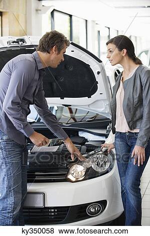 Couple looking at car engine in showroom View Large Photo Image Stock Photo - Couple looking at car engine in showroom. Fotosearch