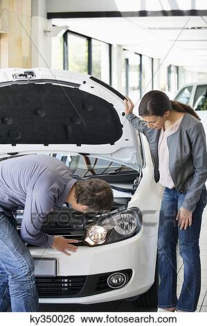 Stock Photograph - Couple looking at car engine in showroom. Fotosearch