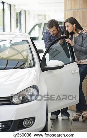 Couple looking inside car at showroom View Large Photo Image Stock Photograph - Couple looking inside car at showroom. Fotosearch