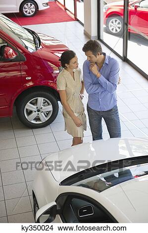 Picture - Female salesperson showing car to mid adult man in showroom. Fotosearch
